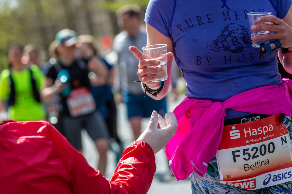 Marathon Verpflegung: Helfer reicht Laufender Getränke beim Haspa Marathon 2022