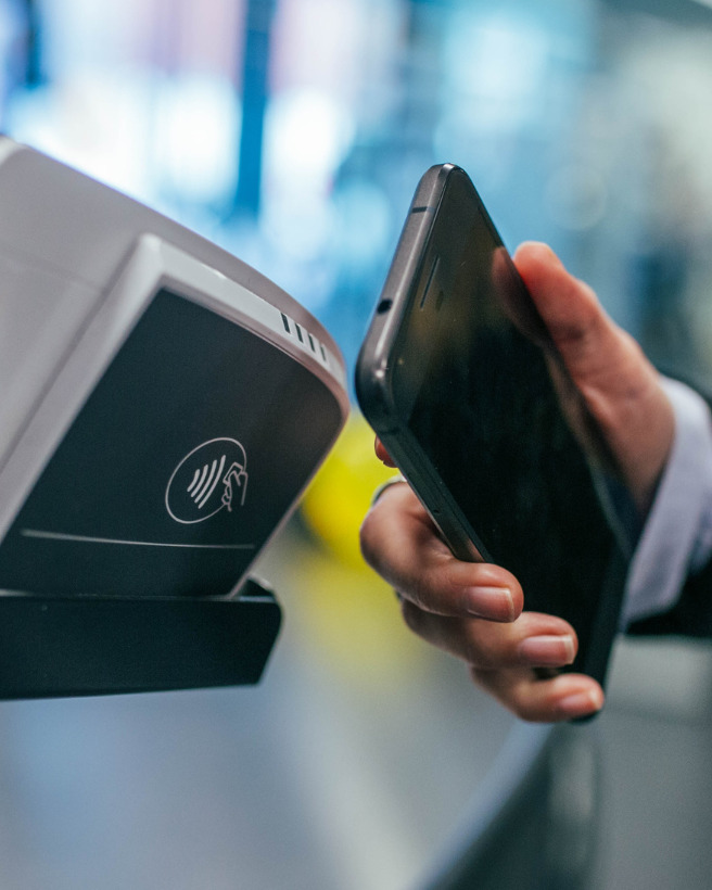 Mobiles Bezahlen: Frau hält Smartphone an ein NFC Gerät
