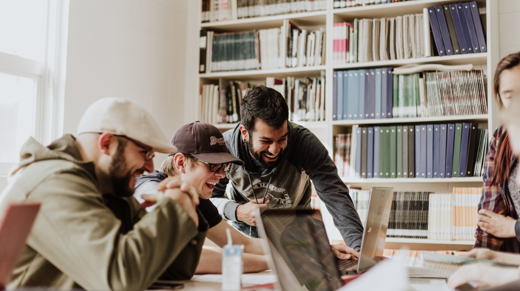 Studienfinanzierung: Mehrere Freunde um einen Tisch herum sitzend und lachend