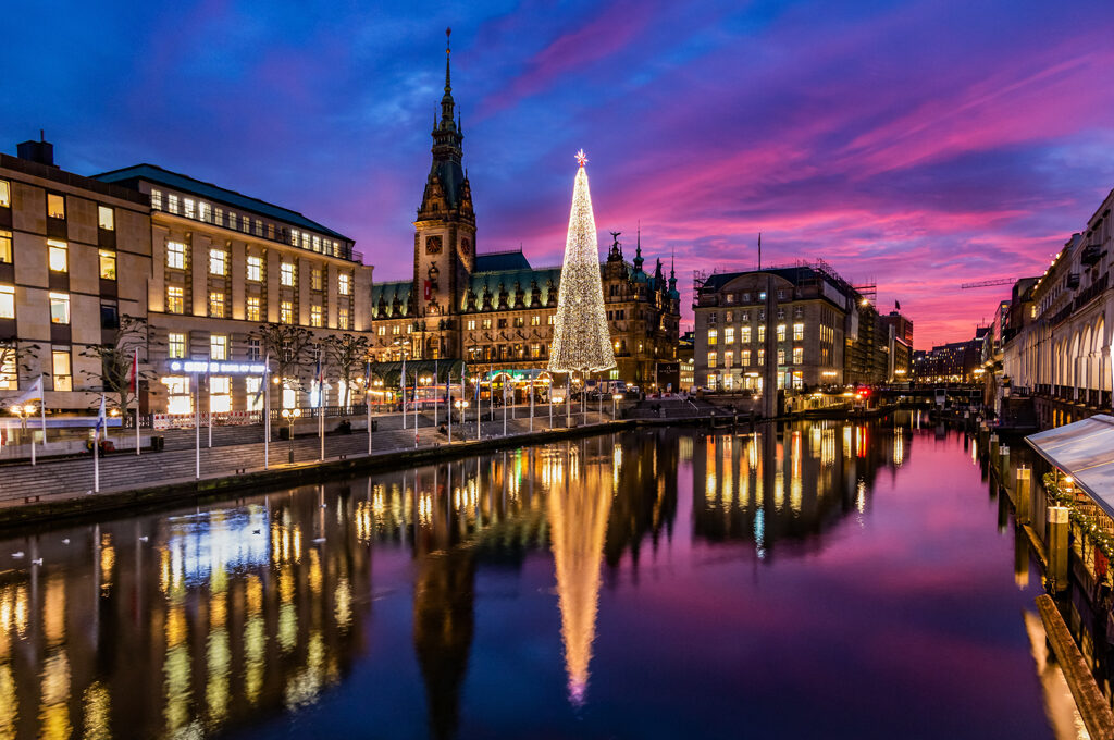 Veranstaltungen in Hamburg: Blick vom Jungfernstieg auf das Hamburger rathaus und den Weihnachtsmarkt im Sonnenuntergang.