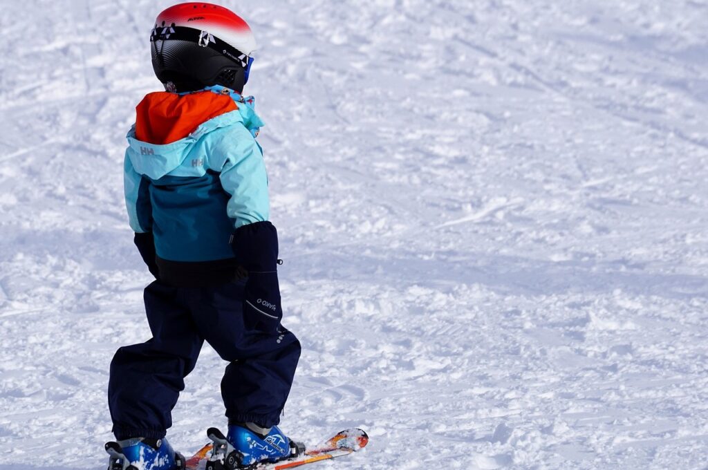 Wintersport in Hamburg: Kind in blauem Skianzug und mit rotem Helm auf Skiern steht auf Abfahrt