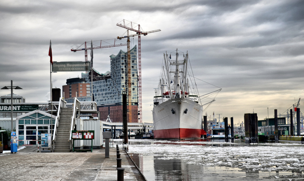 Hamburg Hafen: Das Foto ist von den St.-Pauli-Landungsbrücken in Hamburg aufgenommen und zeigt das Museumsschiff Cap San Diego mit der Elbphilharmonie im Hintergrund. Auf dem Hafenwasser sind stellenweise kleine Eisschollen zu sehen.