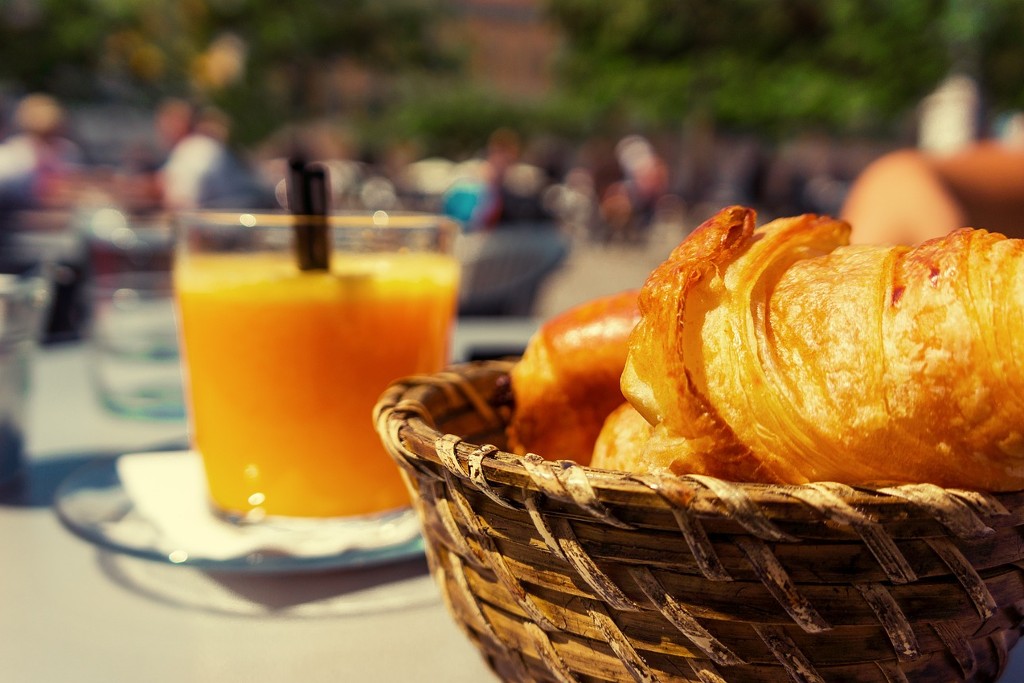 Frühstück am Wasser in Hamburg: Croissants im Holzkörbchen, ein Glas Orangensaft im Hintergrund im sonnigen Café