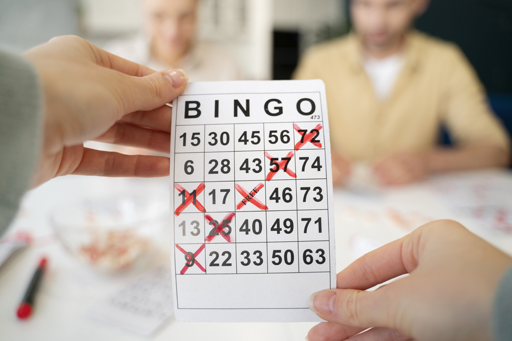 Hamburg im Februar: Hände halten Bingoschein mit roten Kreuzen fest. Zwei Personen sind dahinter unscharf zu erkennen.