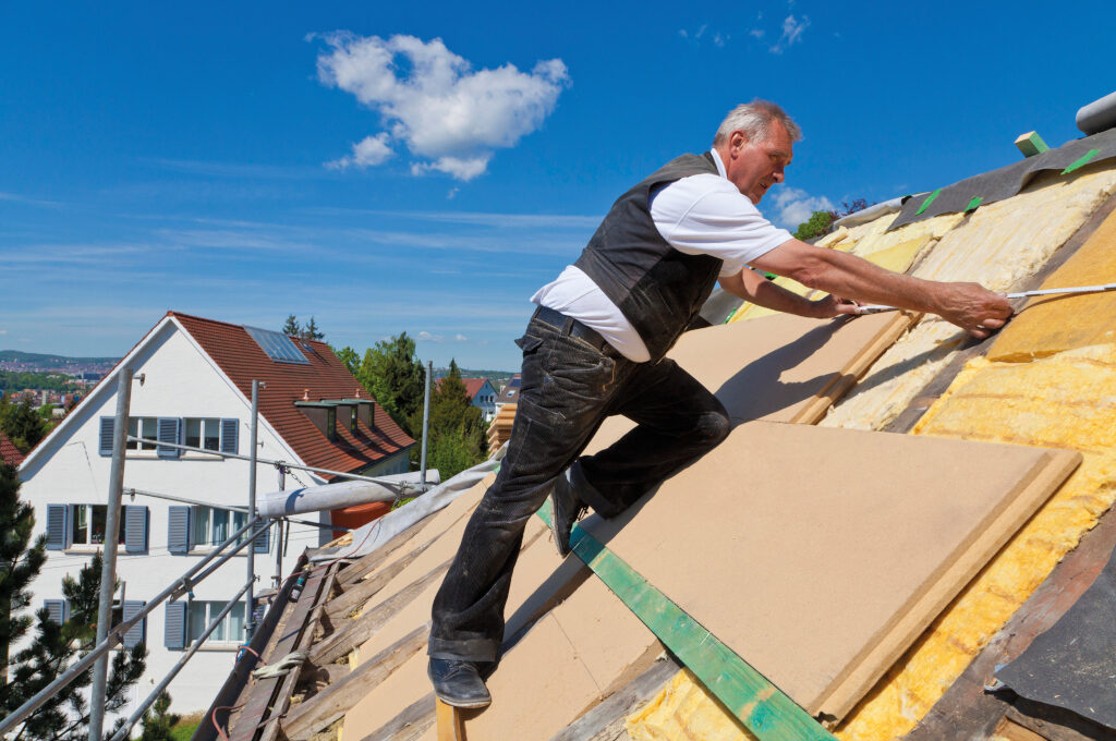 Dachdämmung Kosten: ein Dachdecker verlegt Holzdämmplatten auf einem Dach