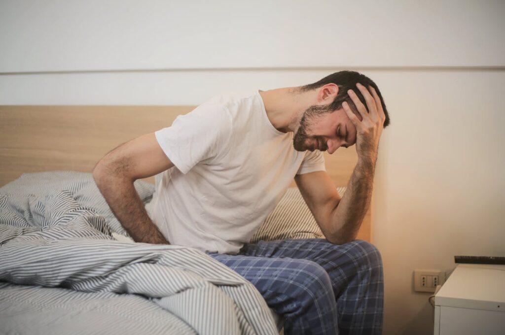 Krangengeld: Ein kranker Mann sitzt auf dem Bett und hält sich erschöpft die Stirn