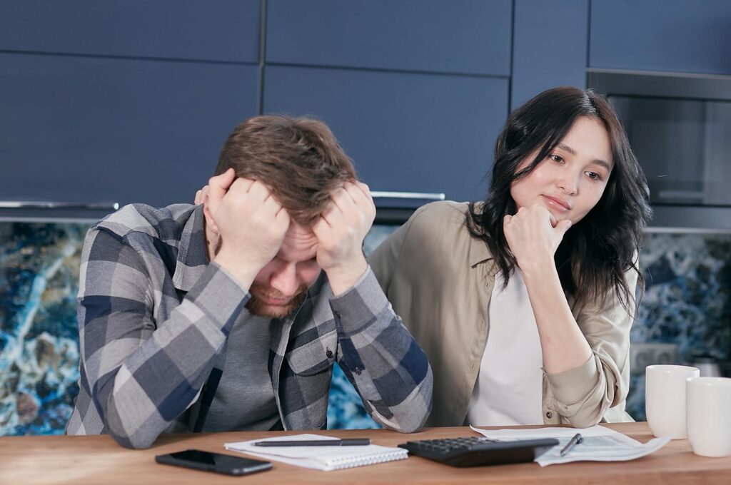 Erbe & Erbschaft: Ein Mann und eine Frau sitzen an einem Tisch und schauen traurig drein