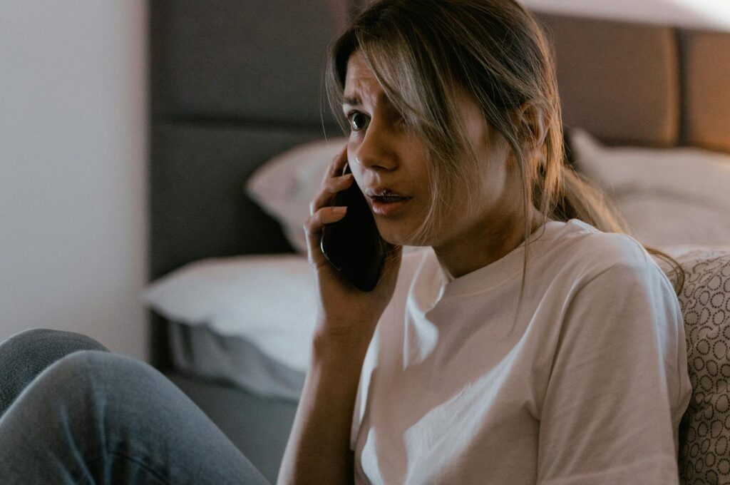 Hotline-betrug: Eine Frau hat ihr Handy am Ohr und schaut schockiert.