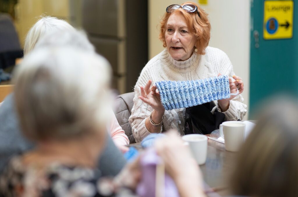Stricken in Hamburg, ältere Frau zeigt ihr Strickprojekt anderen Frauen