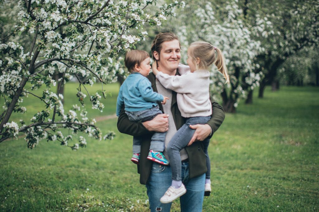 Kinderzuschlag, ein Mann trägt ein kleines Mädchen und einen Jungen auf beiden Armen