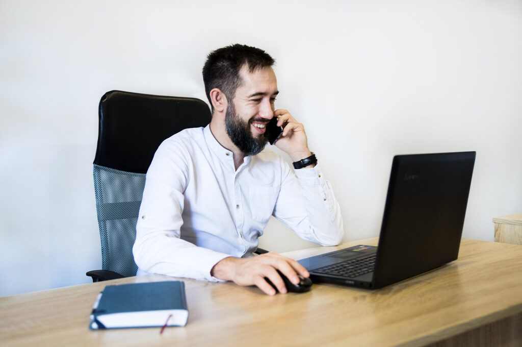 falscher Bankmitarbeiter, Mann mit Handy guckt aufs Notebook