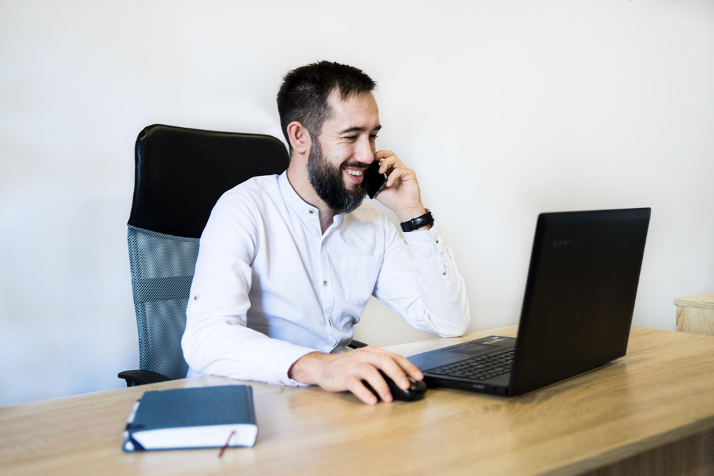 falscher Bankmitarbeiter, Mann mit Handy guckt aufs Notebook
