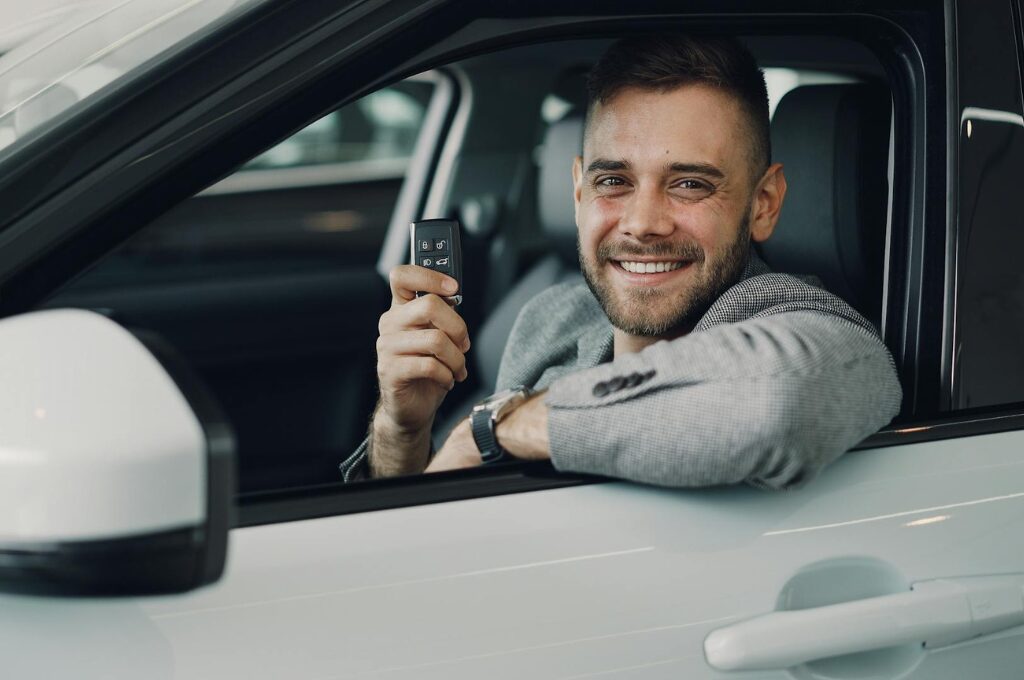 Carsharing: Ein Mann sitzt in einem Auto und präsentiert den Schlüssel