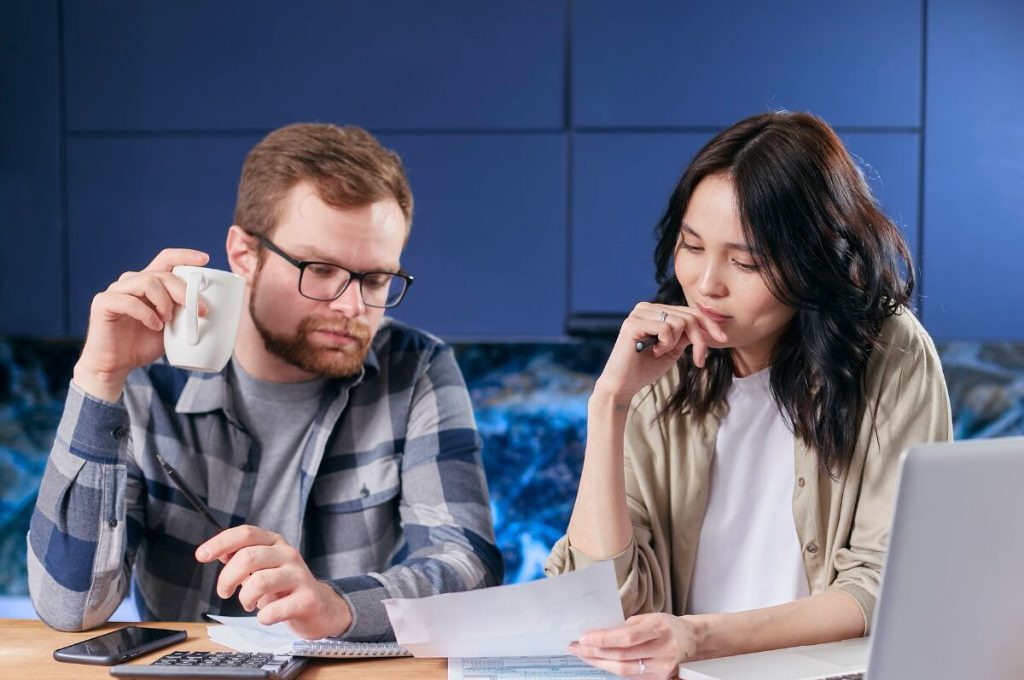 Lifestyle-Inflation, Paar sitzt am Tisch und schaut auf ein Blatt Papier