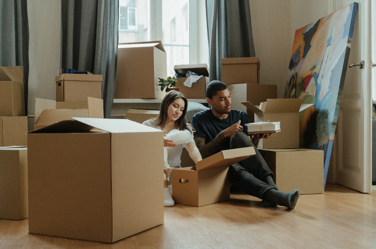 Umzug planen, Paar sitzt auf dem Wohnung und packt Kartons aus