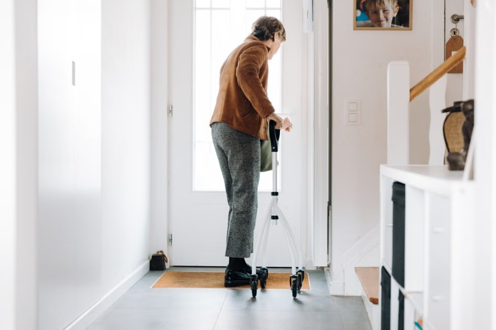 Ältere Dame mit Gehhilfe verlässt das Haus.